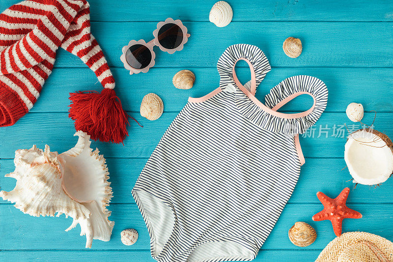 泳衣和圣诞帽旁边的海滩饰品被贝壳包围，海星在绿松石的木制背景上。夏天的氛围在冬天和圣诞假期的海边概念
