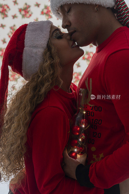 一对拉美裔黑人夫妇穿着红色的圣诞麻袋，戴着圣诞帽，背景是白色的铃铛，他们戴着圣诞帽站在一起，互相表达爱意