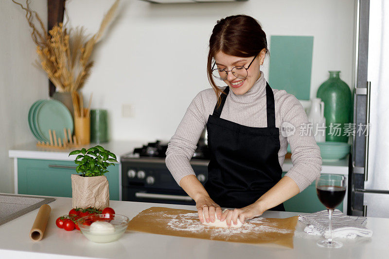 一个穿黑色围裙的女人在厨房里准备面团。