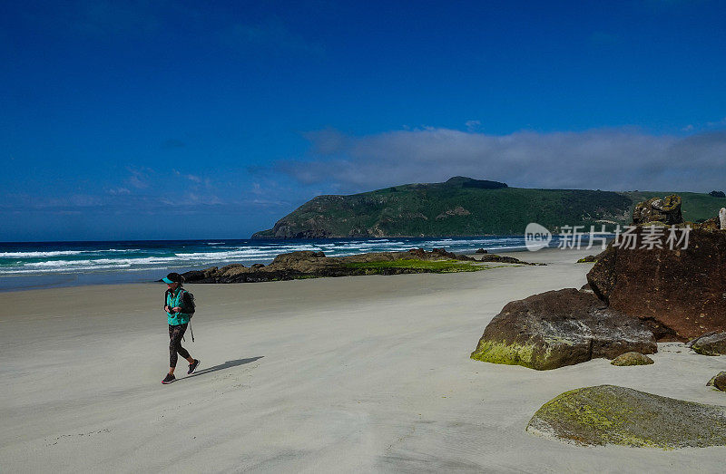 成熟的女子沿着奥塔哥，新西兰海滩徒步旅行。