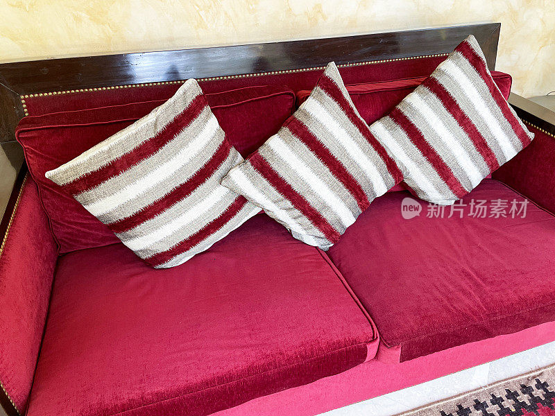 红色天鹅绒软垫沙发的全帧图像与三个红，白，灰，条纹方形靠垫，抬高的观点，重点在前景