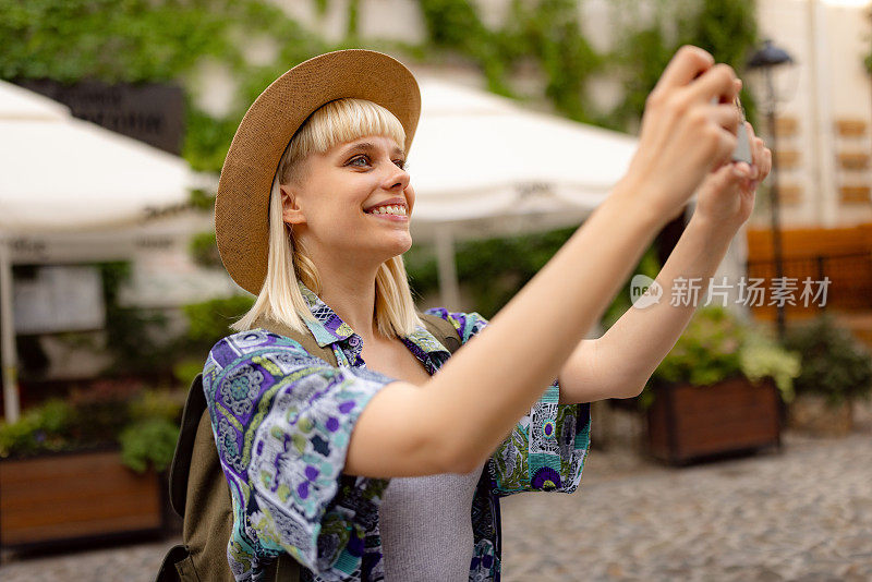 开心的女游客在街上用手机拍照。