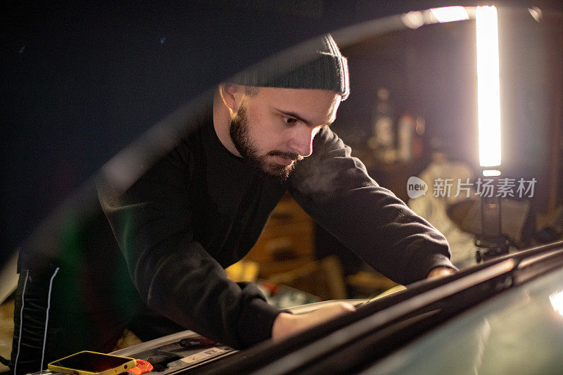 一个年轻人在他的车库里自己维修他的车。