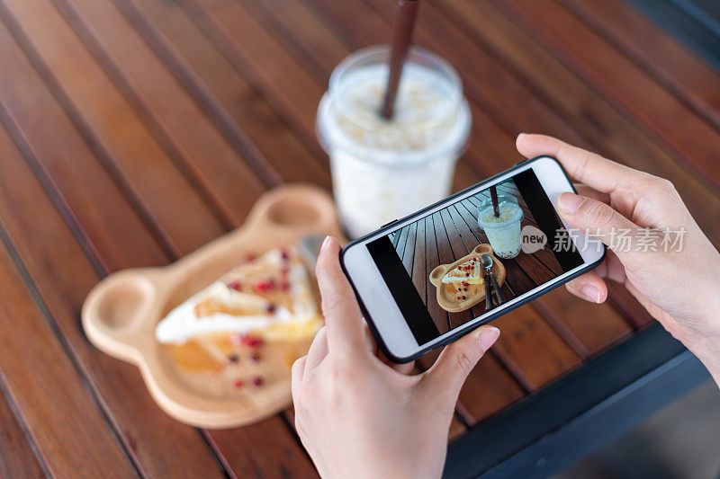 女性们正在用智能手机专注于拍摄咖啡店里的零食和水。女性会为社交媒体更新或餐厅评论拍照。
