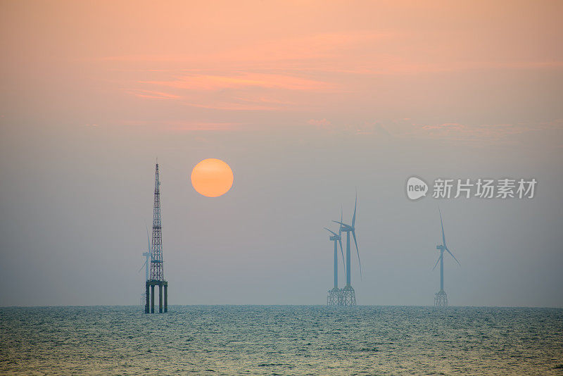风力涡轮机的风扇在波光粼粼的海面上旋转。黄昏时橙红色的太阳。