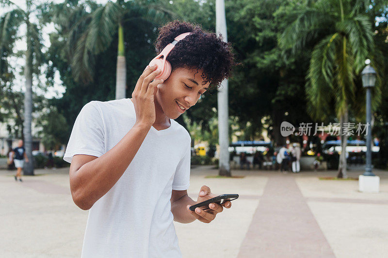 年轻的黑人男子在拉丁美洲阳光明媚的加勒比海城市使用手机和耳机，非洲裔美国人
