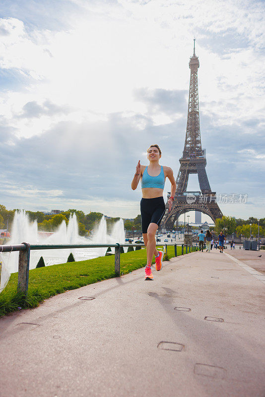 运动的年轻女子在半空中，在巴黎埃菲尔铁塔附近喷泉旁的小路上慢跑