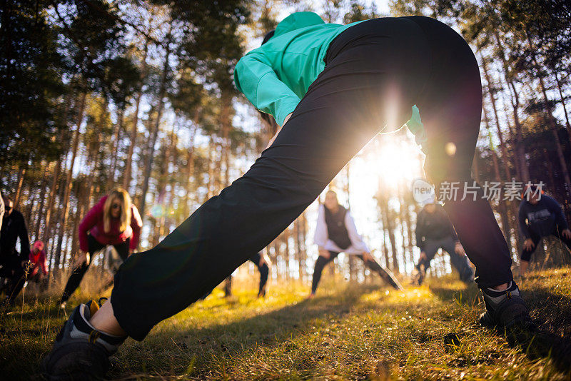 一群白种人，伸展身体，在森林教练带领的集体健身课