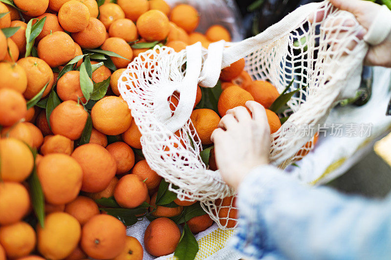 年轻的成年妇女用可重复使用的袋子在市场上买橘子