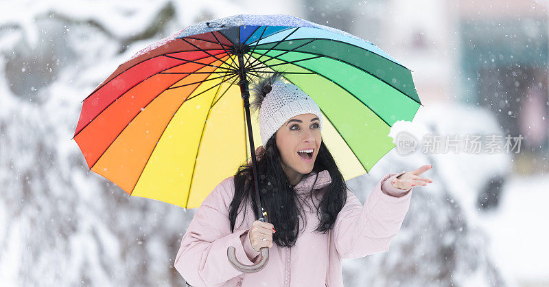 快乐的女人在寒冷的下雪天撑着伞，洒下新鲜的雪