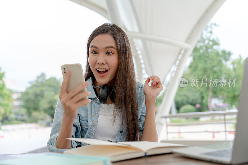 惊讶的表情，哇。快乐的亚洲女学生对智能手机的成功感到兴奋。屏幕显示在手机上显示成功，奖励，奖金，获得促销，获胜者，获胜，折扣购物。肖像
