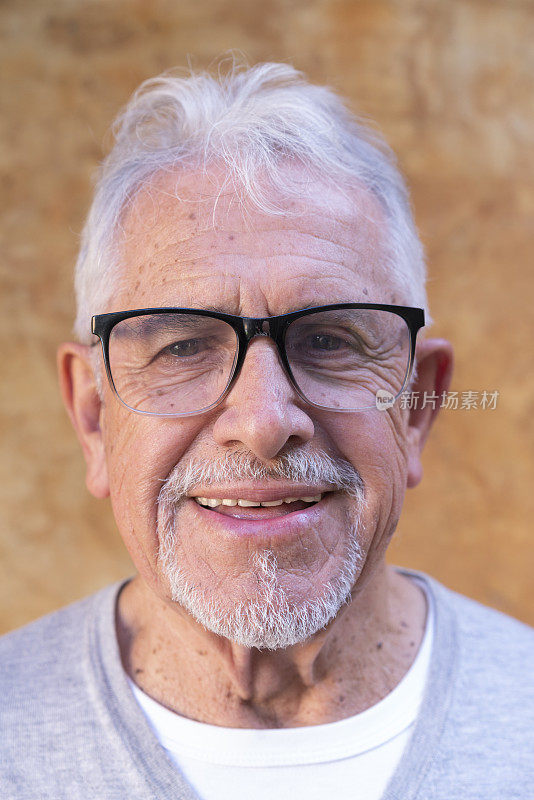 在户外墙壁背景前，一个戴着眼镜微笑的快乐成熟男人的肖像