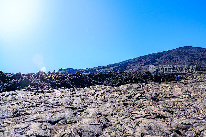 游客在山顶下面的自然火山景观中看着凝固的黑色快速流动的熔岩流。欧洲法国留尼汪岛的富尔奈斯峰。