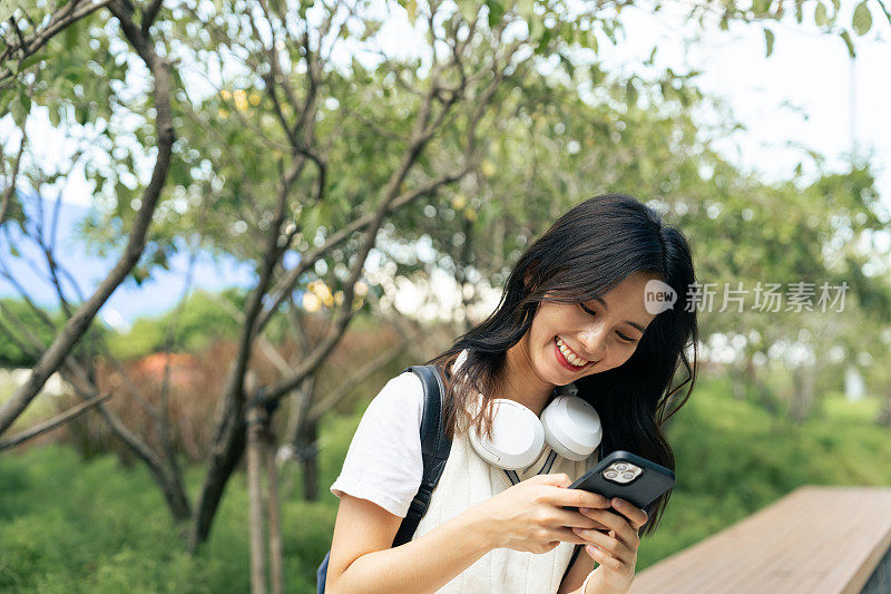 微笑的女人用智能手机和耳机拥抱大自然的旋律