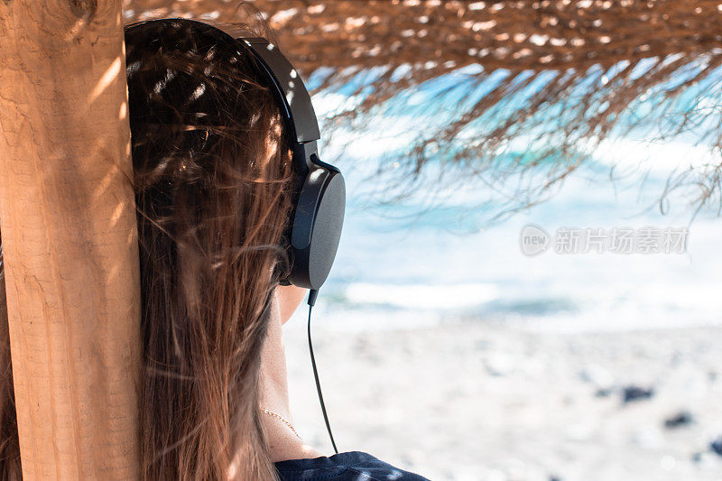 女孩撑着伞在沙滩上听音乐，看着大海