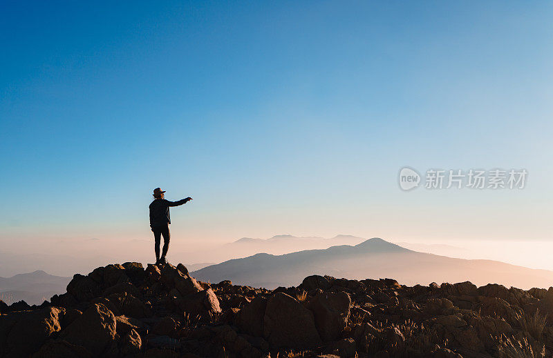 一个登山妇女的剪影在山顶上看日出