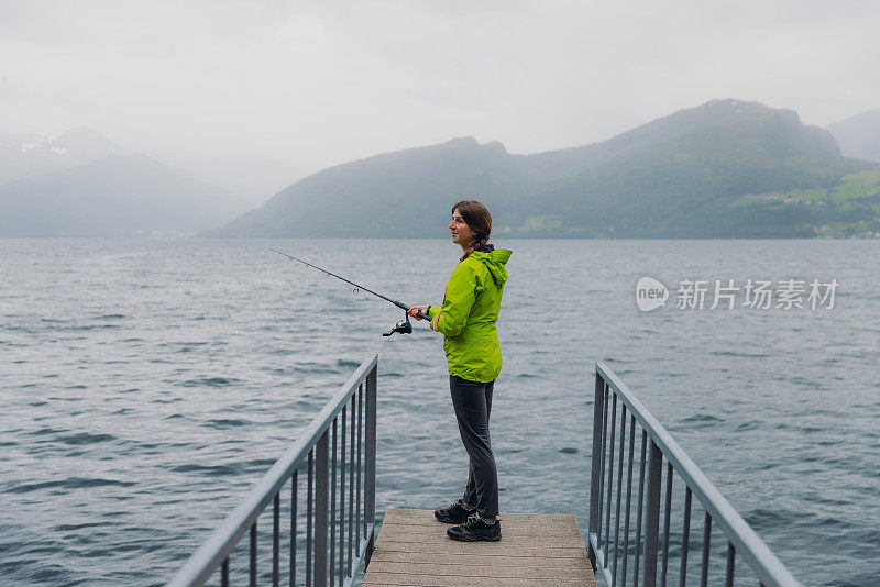 身穿绿夹克的女子在挪威峡湾钓鱼