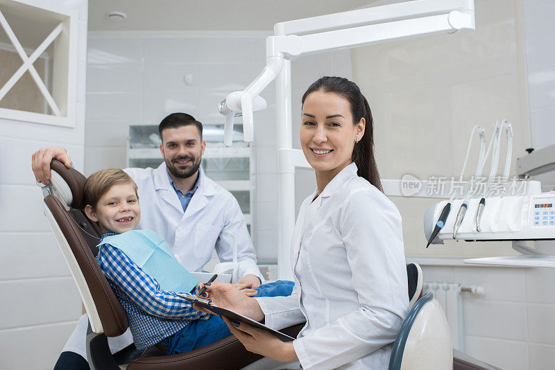 快乐的女牙医和她的助手与快乐的小病人一起工作