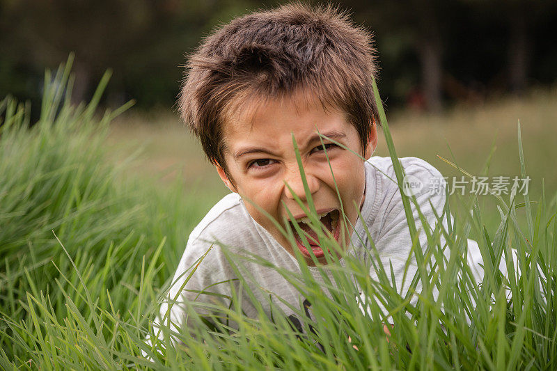 快乐童年的概念，探索你身边的世界。白天，可爱又有趣的男孩在公园的草地上玩捉迷藏。