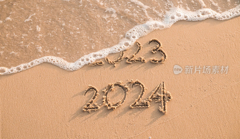 日落时分，海滩上手写的2023和2024字样。“2023再见，2024新年快乐”的概念