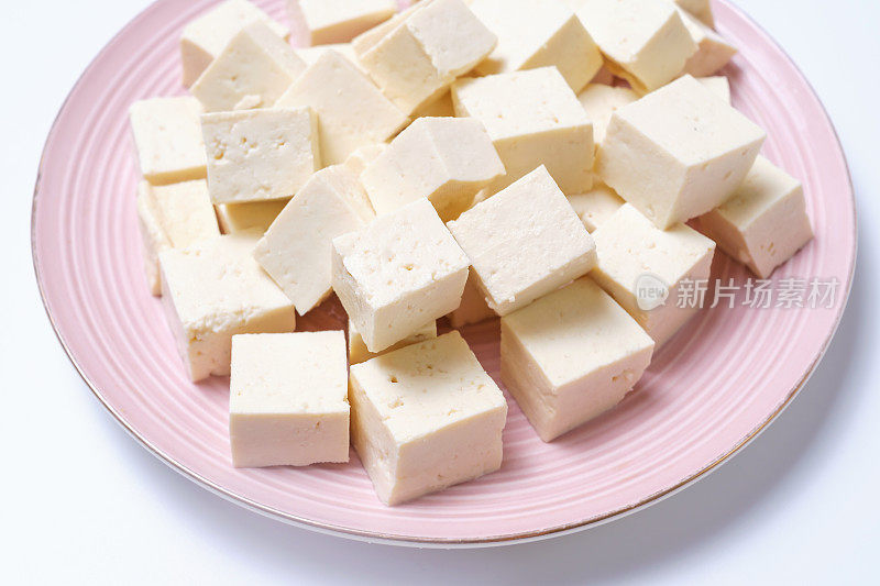 在白色背景的粉色盘子上切豆腐块。
