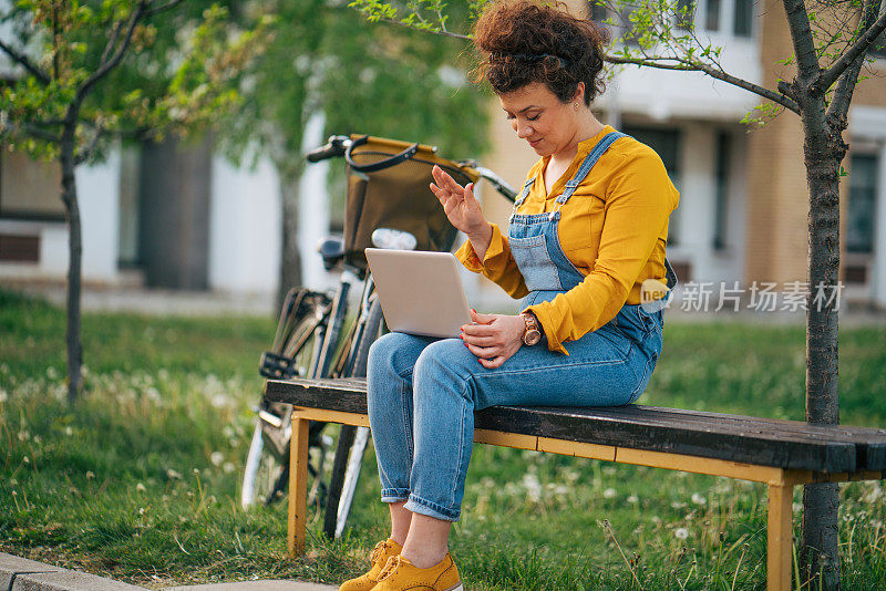 一名女子在进行在线视频通话时向坐在长凳上的笔记本电脑挥手