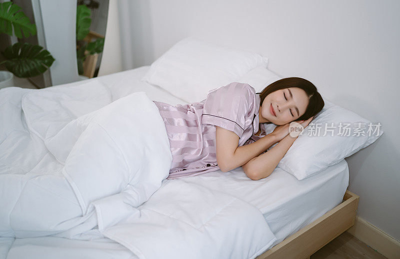 俯视图美丽的年轻亚洲女子微笑穿着缎面睡衣，而睡在床上，放松在早上。女士享受甜蜜的梦，在家里好好休息和平静的气氛。生活方式的概念