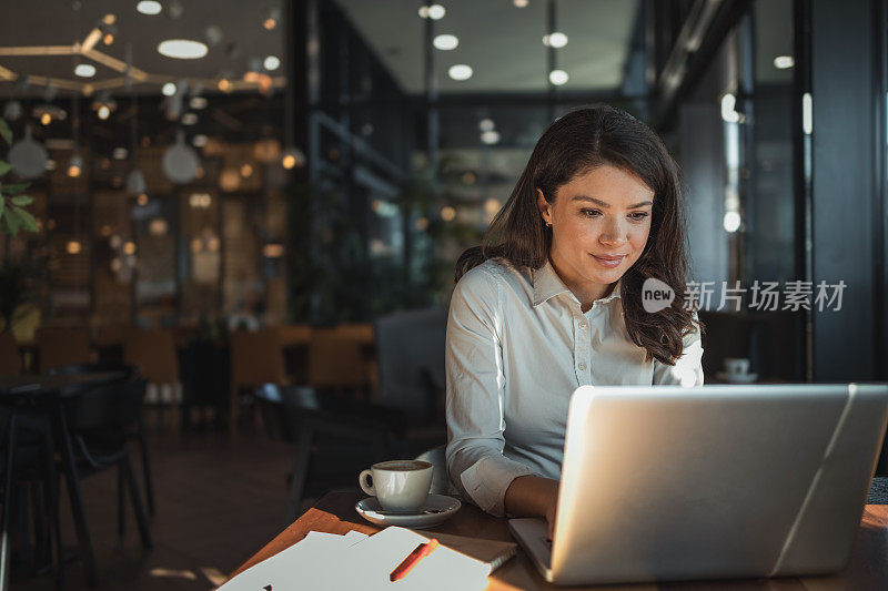 一位美丽的女商人坐在咖啡馆里，用笔记本电脑享受着她最喜欢的咖啡