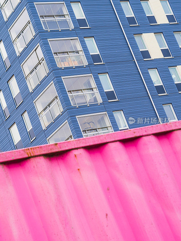 高大的蓝色建筑旁边是粉红色的集装箱