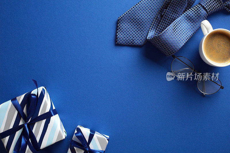 在深蓝色的背景上，用老式的礼品盒、咖啡杯、领带、眼镜平铺构图。父亲节快乐概念