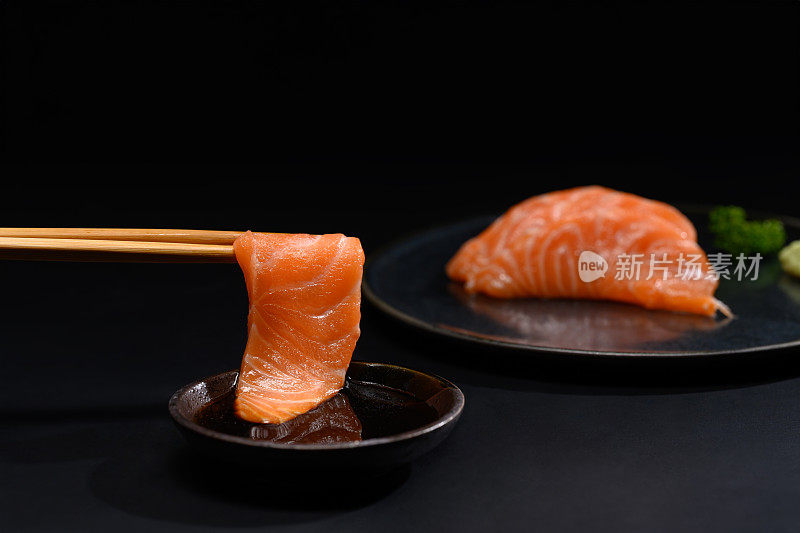 特写筷子与新鲜鲑鱼刺身蘸酱油。日式料理