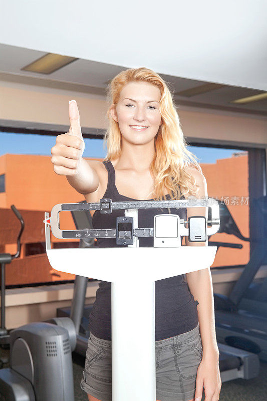 一个女人在健身房的体重秤上竖起大拇指