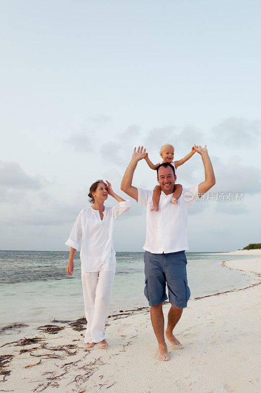 一对夫妇带着一个孩子沿着加勒比海海滩海岸线散步