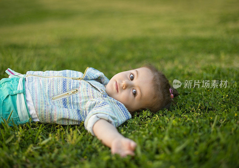 可爱的小孩躺在草地上，看着相机