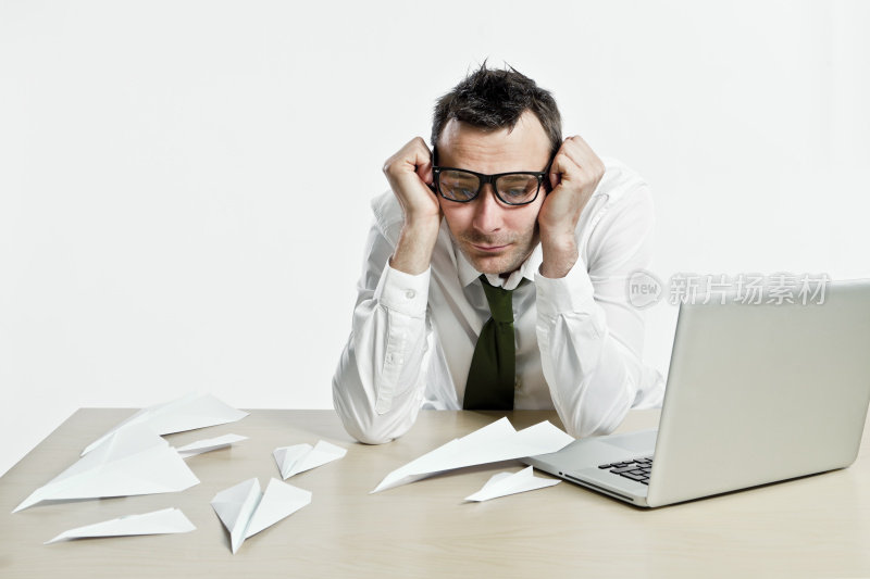 一名办公室职员沉浸在手提电脑和纸飞机的思绪中