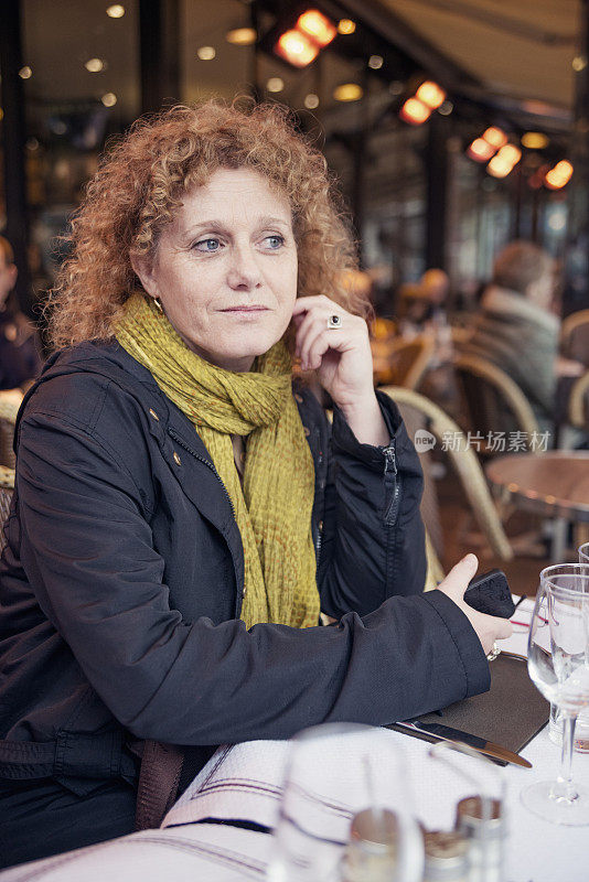 一个成熟的女人独自坐在法国餐厅的露台上。