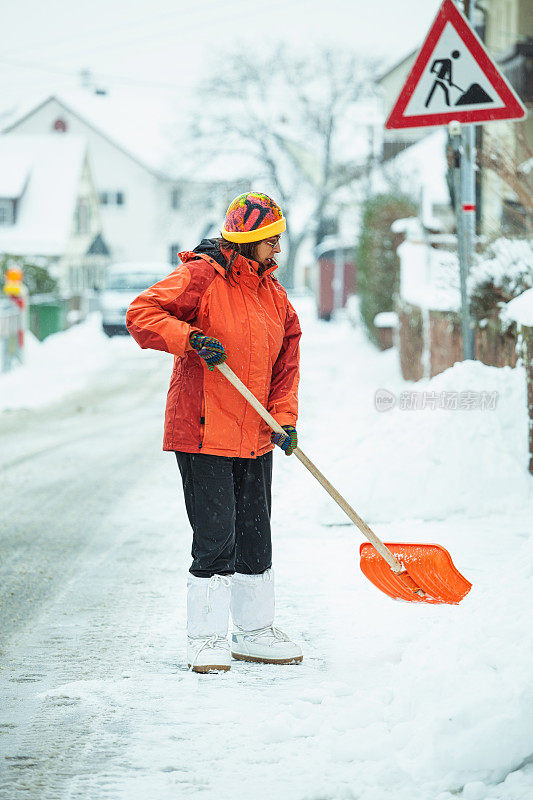 一个成熟的女人在清扫屋前的积雪