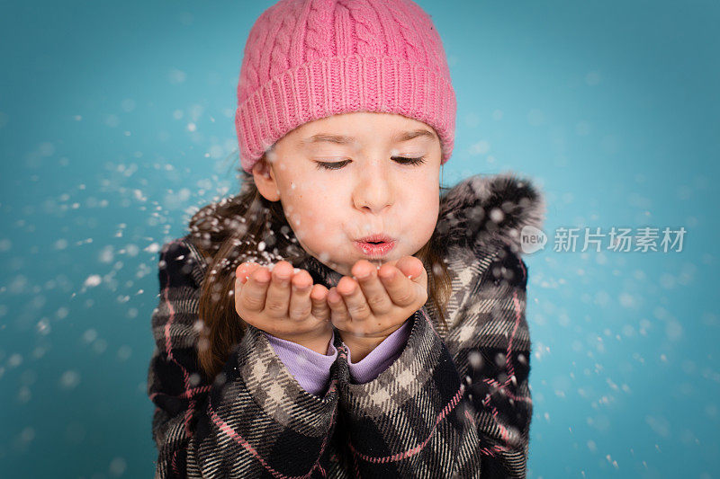 快乐的小女孩向相机吹了一把雪