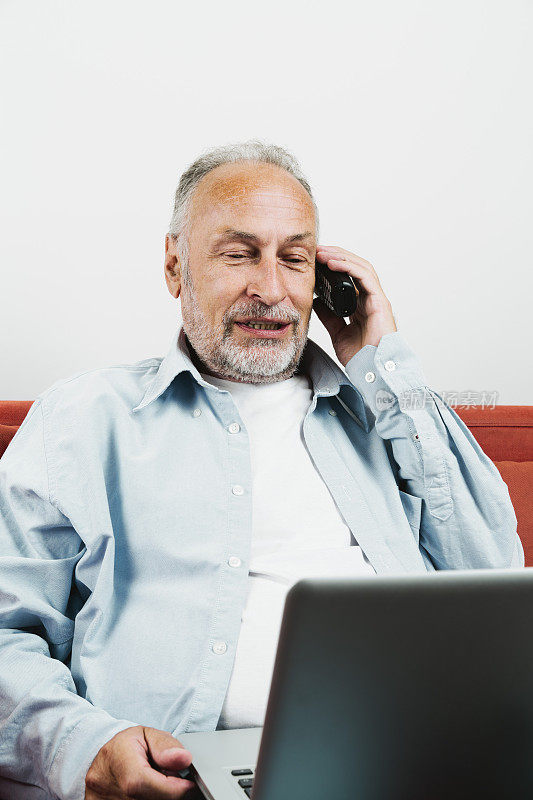 一个老男人坐在那儿，腿上放着笔记本电脑，用手机聊天