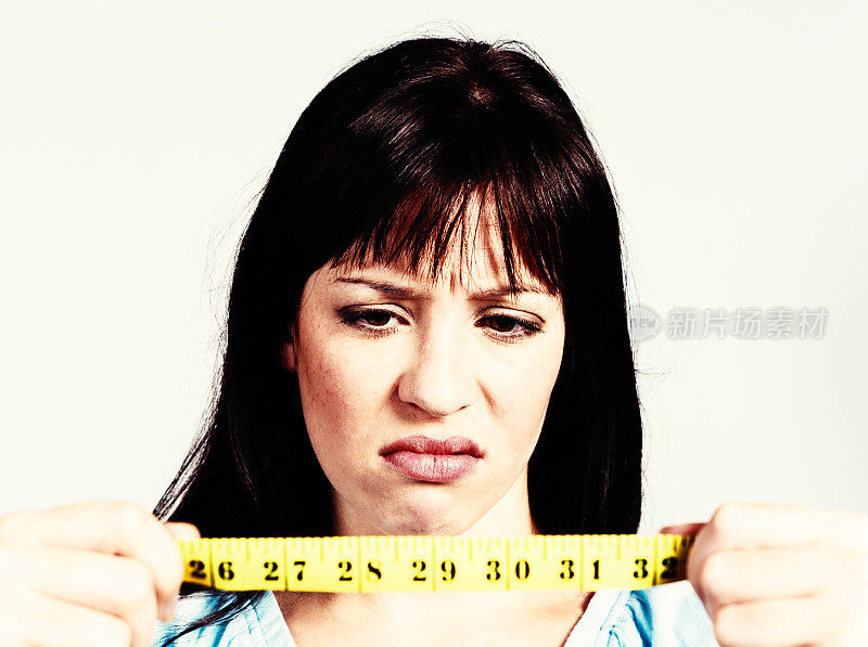 抑郁的女人在卷尺上看英寸:节食失败。