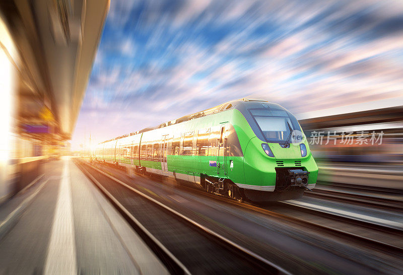 日落时分，欧洲火车站上运行的高速列车。美丽的绿色现代火车在铁路站台与运动模糊效果。铁路上有客运列车的工业场景