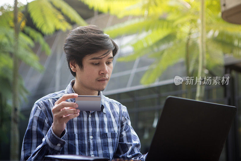 东南亚帅哥穿着衬衫在咖啡馆用智能手机，手里拿着信用卡，在户外网上购物