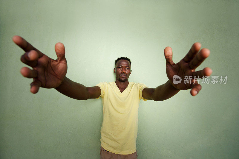 一个非洲人伸出双臂，靠在绿色的墙上