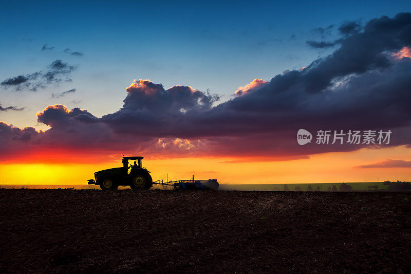 农民的剪影在拖拉机准备土地与苗床中耕，日落拍摄