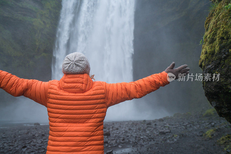 在冰岛旅游的女游客站在壮丽的瀑布旁，张开双臂拥抱大自然，人们旅游冒险的概念