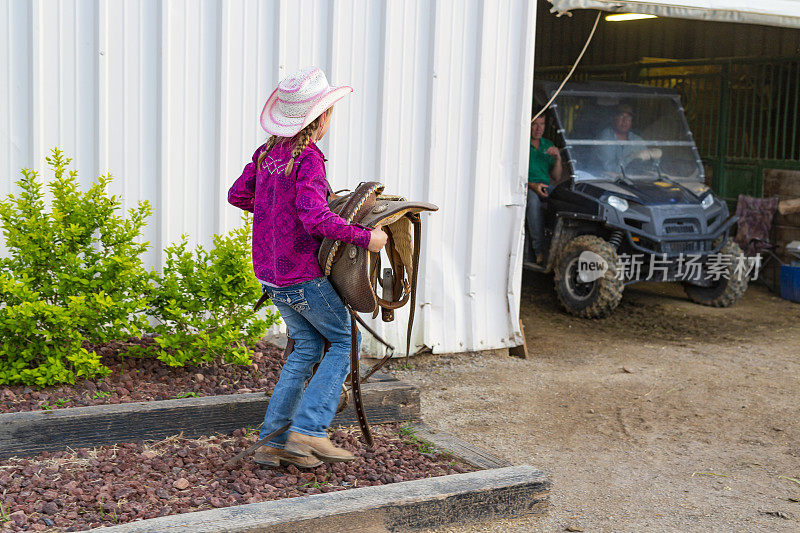 年轻的女牛仔在骑马后收起她的马鞍