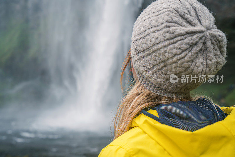 女游客在冰岛旅游时，站在壮丽的瀑布旁边，沉思大自然，人们旅行冒险的概念