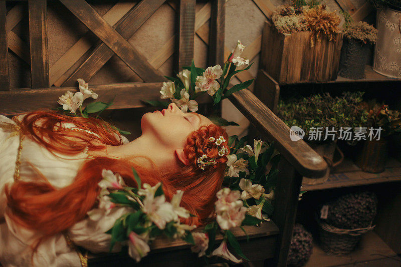 美丽的红头发女孩躺在花丛中