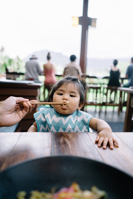 蹒跚学步的孩子坐在餐厅的高椅子上用筷子喂食食物