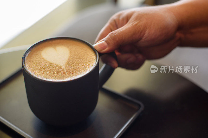 男人的手拿起一杯带有心形泡沫的咖啡